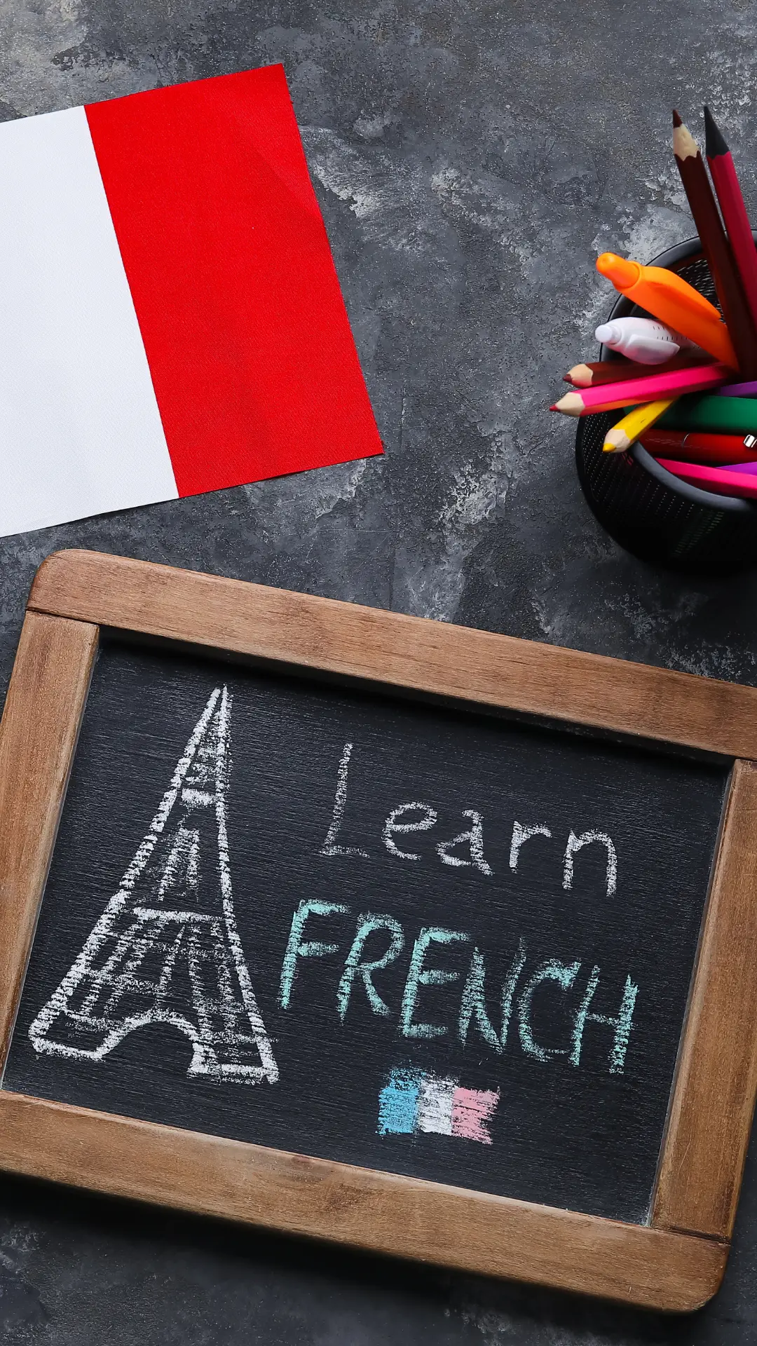 Une ardoise où est écrit « Learn French », un drapeau français et des crayons de couleur